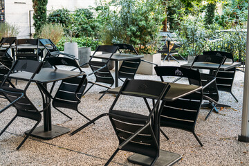 Empty outdoor cafe terrace with black metal chairs scattered around square tables. Urban greening, climate-conscious public design, European street culture, sustainability