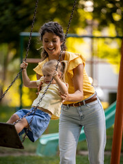 Girl standing and swinging on playground as mom holds her up