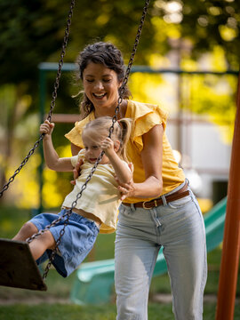 Girl standing and swinging on playground as mom holds her up