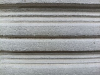close-up view of a pale white pillar. Made of cement and lime mixture and patterned with horizontal lines with shallow grooves downwards