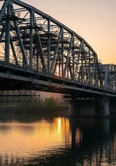 Naklejka premium Sunset over a industrial bridge reflecting in calm waters near a city at twilight