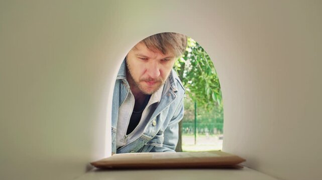 Man in denim jacket picking up stack on letters from mailbox while standing outside on summer day