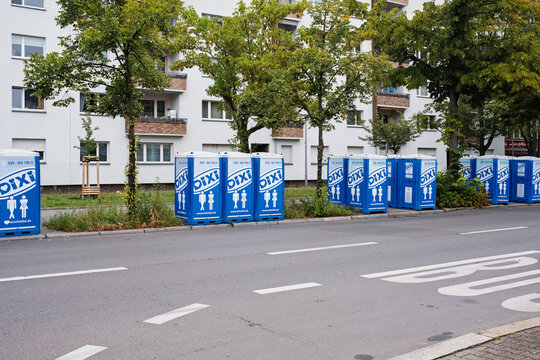 Row of blue portable toilets lined up along a residential street with apartment buildings in the background
