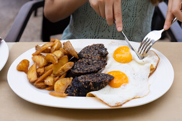 Girl eating spanish food, fried black sausage from Burgos made of blood and rice, served with french fries potato and fried eggs.