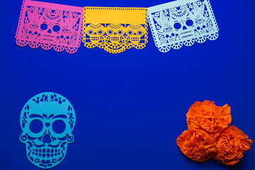 Day of the Dead decorations with colorful papel picado and marigold flowers. On a blue background