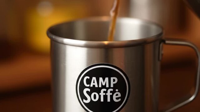 Pouring Coffee into Metal Camp Mug - Close-up shot of coffee pouring into a stainless steel camping mug. The mug features a circular logo that reads "Camp Soffe".