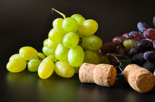 Bunches of white and blue grapes with champagne corks on black background - Powered by Adobe