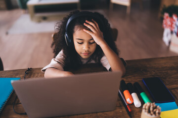 Focused black girl using laptop and headphones in living room