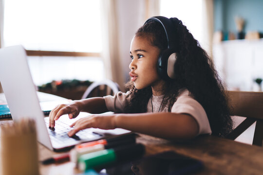 Smiling ethnic girl using laptop by table in living room