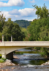 Looking down a stream as water flows under an arched white bridge with a blue sky and fluffy clouds