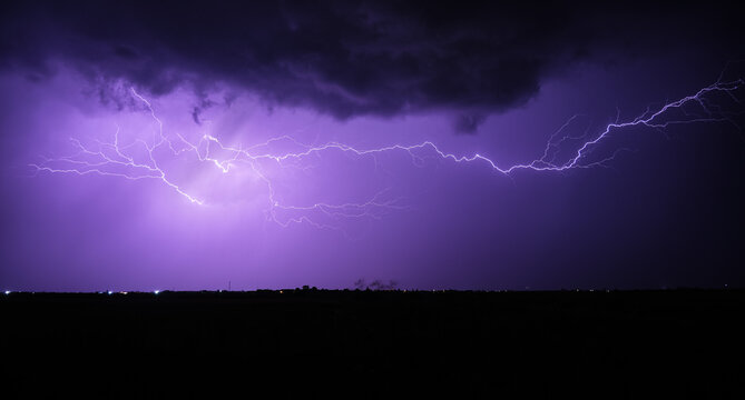 Vivid and dynamic display of lightning across a purple night sky above a dark landscape, showcasing nature's power and beauty. - Powered by Adobe