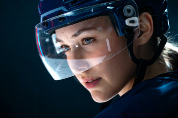 Close-up portrait of female ice hockey player wearing helmet with visor, focused expression before game. Editorial image of women in sports and professional hockey preparation.