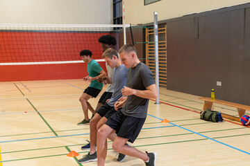 Diverse male players practicing footwork drills at gym using orange cones beside volleyball net