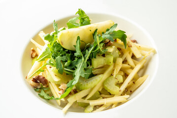 Fresh salad with green apple slices, celery, arugula, and walnuts in a white bowl. Healthy vegetarian dish with crisp textures and natural ingredients. Top view, studio lighting