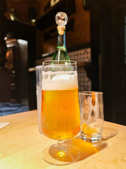 A glass of beer sits on a table next to a bottle