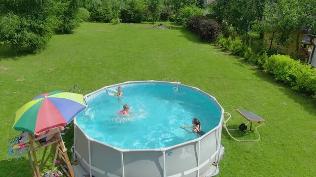 Top-down drone shot of a joyful girl jumping into a frame pool with a big splash. Pure happiness and fun during summer vacation at a country house on a sunny day