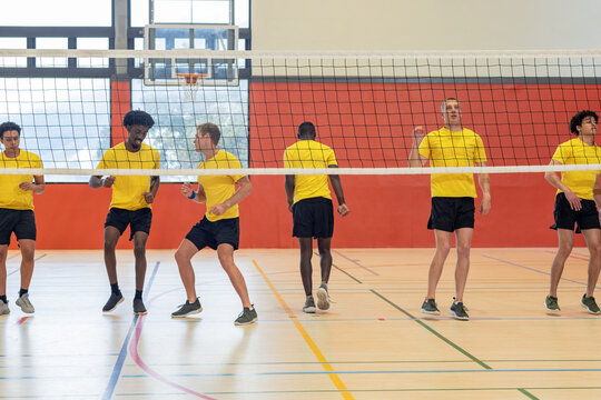Diverse male teammates in yellow shirts practicing blocking drills on court with net, hoop