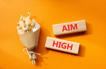 Aim High symbol. Wooden blocks with words Aim High. Beautiful orange background with bouquet of flowers. Business and Aim High concept. Copy space.