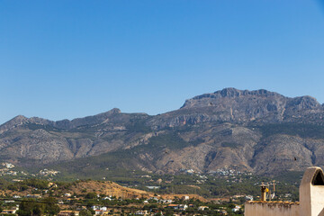 Obraz premium Stunning view of the majestic Puig Campana mountain in Altea, Spain, captured under a clear blue sky. Hills and valleys blend harmoniously, showcasing natures beauty.