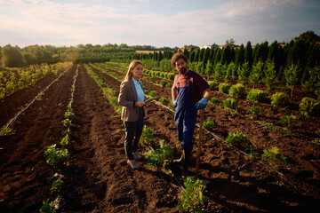 Businesswoman and worker standing among tree seedlings in the field.