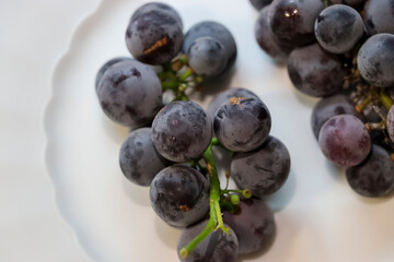 Fresh dark grapes arranged on a white plate, showcasing their rich color and texture. Ideal for healthy eating concepts or food-related articles.