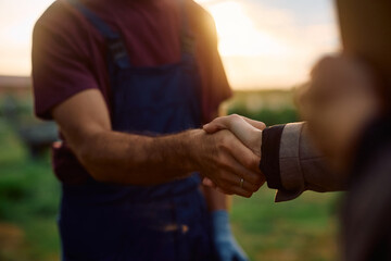 Close up of farm owner and businesswoman shaking hands in the field.