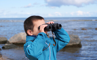 Boy looking through binoculars - A child on an adventure, exploring the horizon and watching something in the distance with binoculars