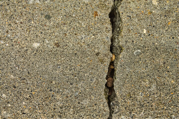 Macro photograph of a deep crack in a gray concrete floor. An abstract grunge texture symbolizing stress, division, damage, structural issues, and risk.