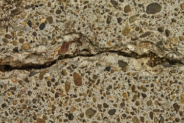 Close-up of a deep crack in a weathered concrete surface with exposed aggregate. Abstract grunge texture background symbolizing damage, stress, aging, and structural problems.