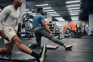 Two male athletes stretching legs in modern gym
