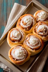 Fototapeta premium Freshly baked cinnamon rolls sit on a metal tray, adorned with whipped cream and chopped nuts. The warm, inviting kitchen background adds to the comforting atmosphere of homemade treats