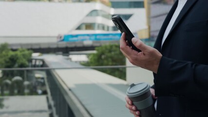 Closeup view of businessman hands holding smartphone and coffee cup in urban district. Male manager checks trade market data via mobile phone walking along street in morning - Powered by Adobe
