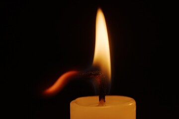 A vibrant candle flame dances in the darkness, casting a warm and inviting glow.