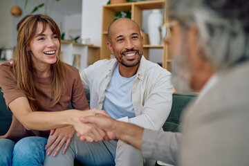 Smiling couple shaking hands with financial advisor during a meeting in the living room at home