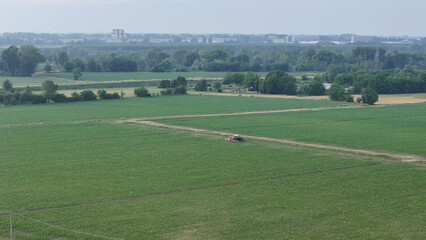 Obraz premium Aerial perspective showcasing a farmer operating a tractor engaged in crop treatment across a vibrant green soybean field embodying sustainable agricultural advancements