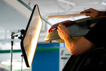 A professional mechanic is repairing a dent on a car's panel in an auto repair shop. A reflective...