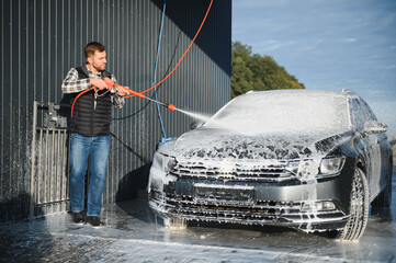Fototapeta na wymiar Car wash equipment. A man is washing a car at self service car wash. High pressure vehicle washer machine sprays foam
