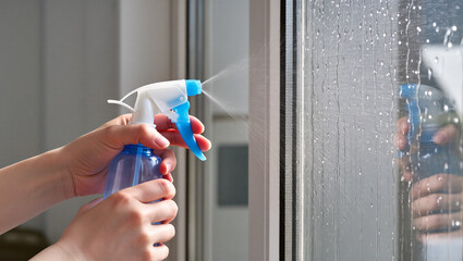 Cleaning window with spray bottle closeup shot of hands