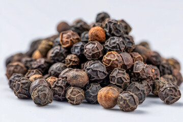 Close-up of whole black peppercorns piled against a light background showcasing the texture and natural color variations of dried spices for culinary use