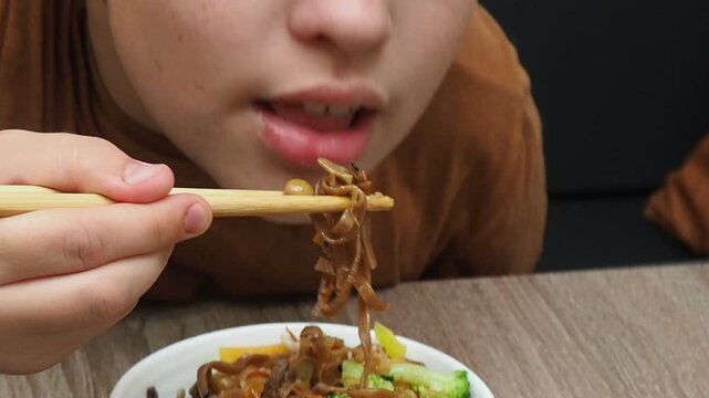 boy eatSchezwan Noodles or Vegetable Hakka Noodles or Chow Mein in white bowl. Schezwan Noodles is indo-chinese cuisine hot dish with udon noodles, vegetables and chilli sauce with meat, Japanese food
