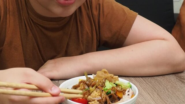boy eatSchezwan Noodles or Vegetable Hakka Noodles or Chow Mein in white bowl. Schezwan Noodles is indo-chinese cuisine hot dish with udon noodles, vegetables and chilli sauce with meat, Japanese food