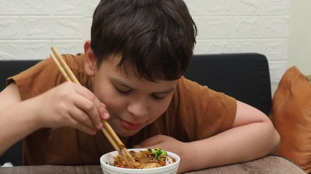 boy eatSchezwan Noodles or Vegetable Hakka Noodles or Chow Mein in white bowl. Schezwan Noodles is indo-chinese cuisine hot dish with udon noodles, vegetables and chilli sauce with meat, Japanese food