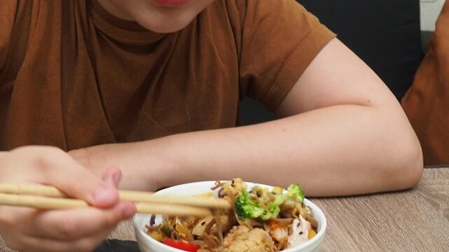 boy eatSchezwan Noodles or Vegetable Hakka Noodles or Chow Mein in white bowl. Schezwan Noodles is indo-chinese cuisine hot dish with udon noodles, vegetables and chilli sauce with meat, Japanese food