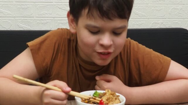 boy eats Schezwan Noodles or Vegetable Hakka Noodles  Chow Mein in white bowl. Schezwan Noodles is indo-chinese cuisine hot dish with udon noodles, vegetables and chilli sauce with meat, Japanese food