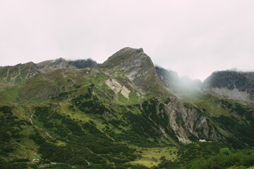 Gr&uuml;ne Almh&auml;nge und schroffe Gipfel unter tiefh&auml;ngenden Wolken in den Alpen