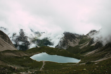Hochalpiner Bergsee umgeben von dramatischer Felslandschaft und Nebelschwaden
