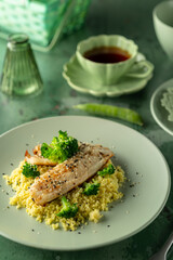 Delicious grilled fish fillet served with couscous, broccoli and sesame seeds on green plate
