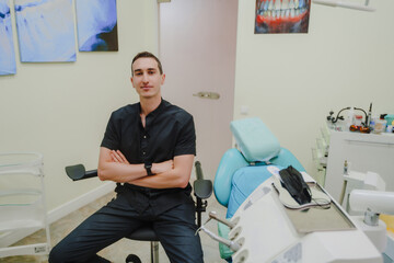 A young dentist at his workplace. Specialist in oral cavity treatment. A doctor in a black uniform. A doctor with a watch on his right hand. Interior of a dental office.