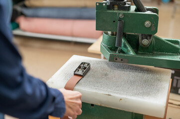 A woman makes holes in a leather belt in a workshop.
