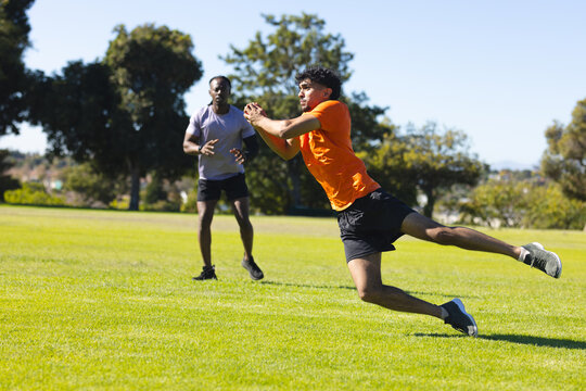 Diverse male friends practicing catching football at urban park wearing sportswear, copy space